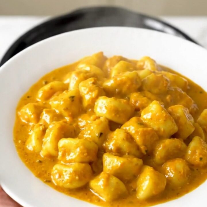 A top-down view of a slow cooker filled with creamy pumpkin alfredo gnocchi on a white speckled countertop.