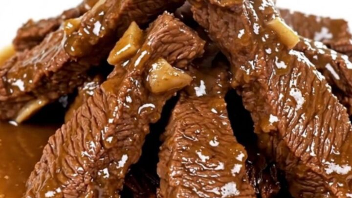A plate of tender, glossy beef tips in a savory herb gravy served on a white plate.