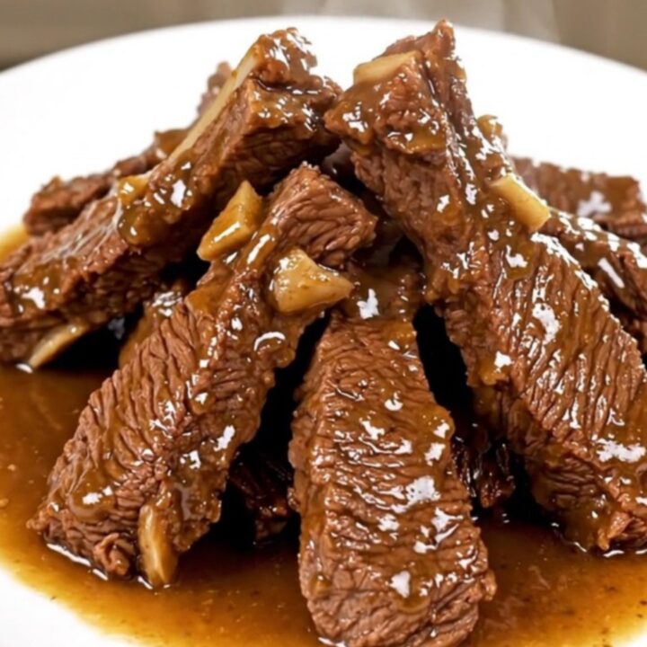 A plate of tender, glossy beef tips in a savory herb gravy served on a white plate.