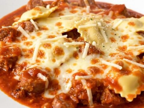 A steaming, hearty serving of Italian sausage and cheese ravioli casserole in a white bowl.