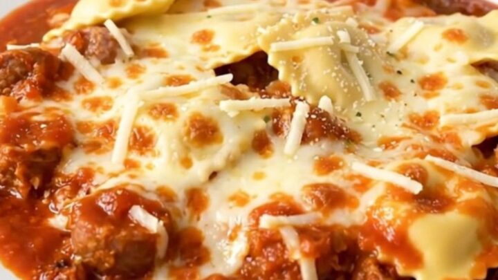 A steaming, hearty serving of Italian sausage and cheese ravioli casserole in a white bowl.