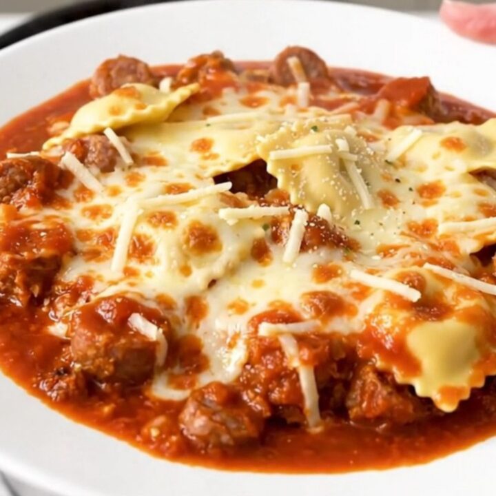 A steaming, hearty serving of Italian sausage and cheese ravioli casserole in a white bowl.