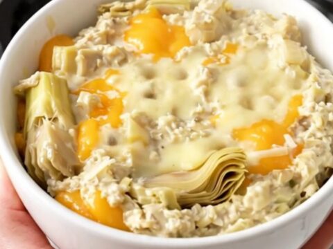 A top-down view of a black slow cooker filled with a creamy artichoke dip on a speckled countertop.