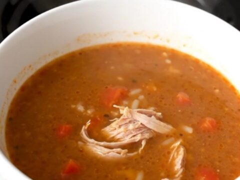A steaming bowl of ground turkey and bell pepper soup in a white bowl on a wooden table.