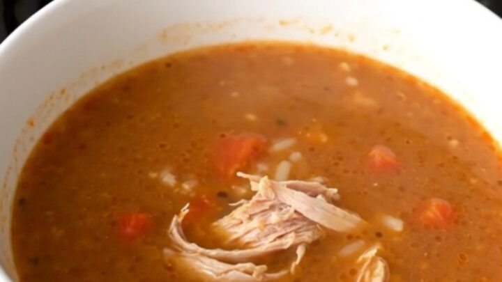A steaming bowl of ground turkey and bell pepper soup in a white bowl on a wooden table.