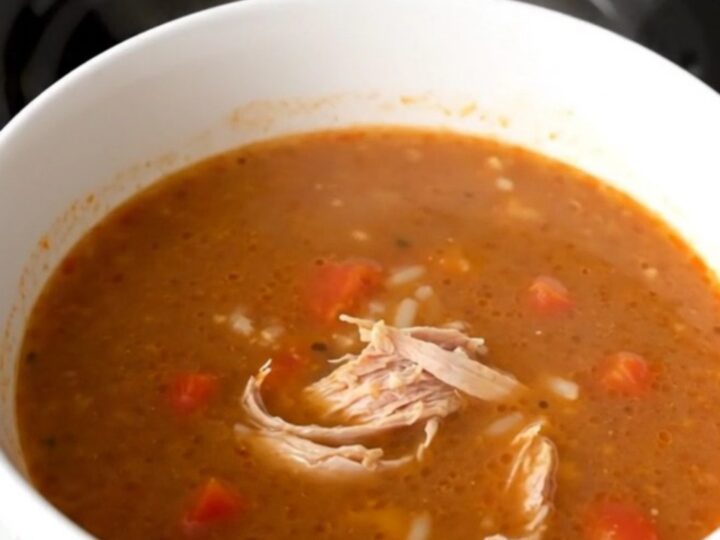 A steaming bowl of ground turkey and bell pepper soup in a white bowl on a wooden table.