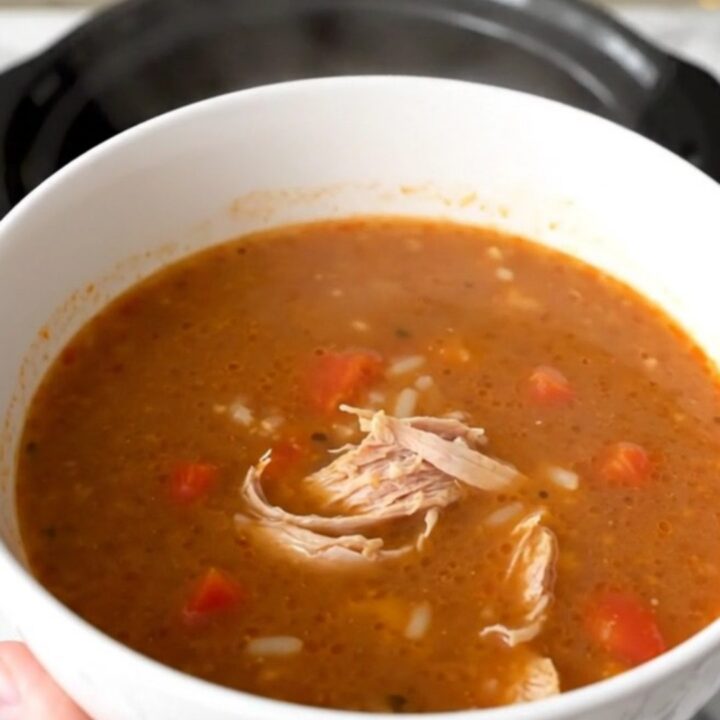A steaming bowl of ground turkey and bell pepper soup in a white bowl on a wooden table.