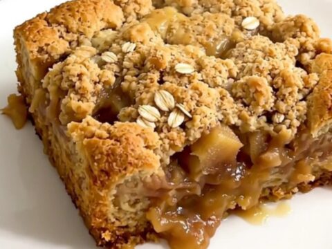A close-up of golden brown apple crisp with melted butterscotch chips served in a white bowl.