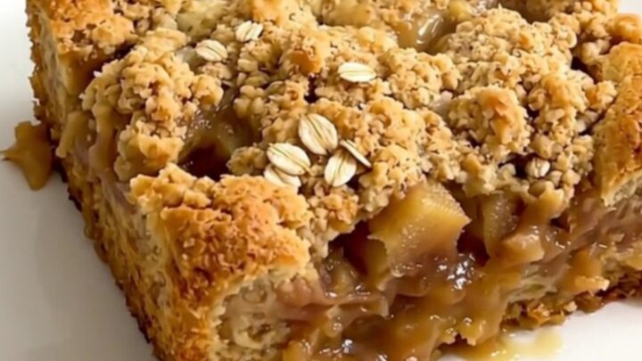 A close-up of golden brown apple crisp with melted butterscotch chips served in a white bowl.