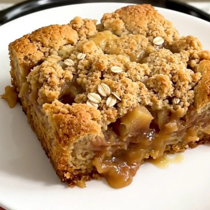 A close-up of golden brown apple crisp with melted butterscotch chips served in a white bowl.