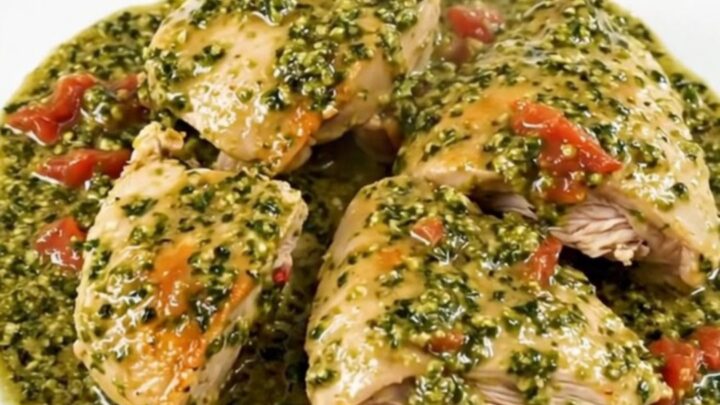 A top-down view of chicken thighs cooking in a slow cooker with pesto and cherry tomatoes.