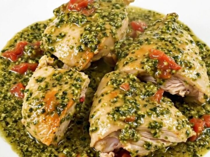 A top-down view of chicken thighs cooking in a slow cooker with pesto and cherry tomatoes.
