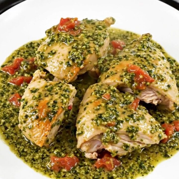 A top-down view of chicken thighs cooking in a slow cooker with pesto and cherry tomatoes.