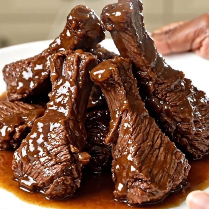 A close-up of tender, glossy chipotle beef tips served on a white plate with bell peppers.