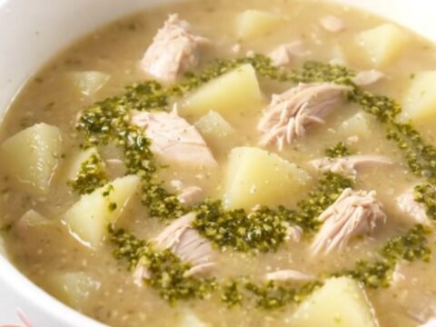 A steaming bowl of creamy pesto chicken chowder served in a white bowl with fresh basil leaves.