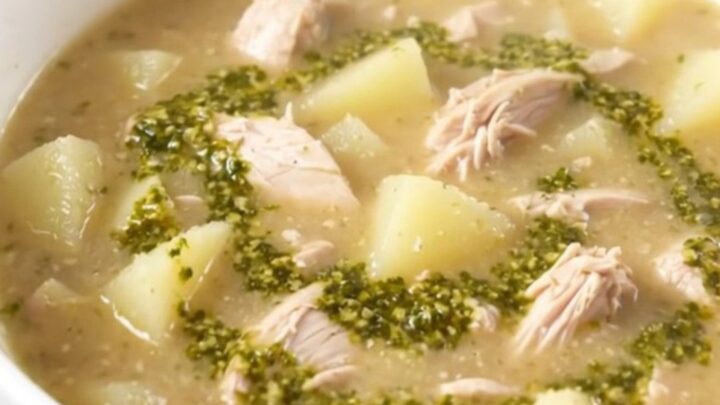 A steaming bowl of creamy pesto chicken chowder served in a white bowl with fresh basil leaves.