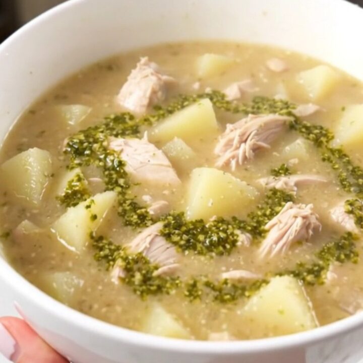 A steaming bowl of creamy pesto chicken chowder served in a white bowl with fresh basil leaves.