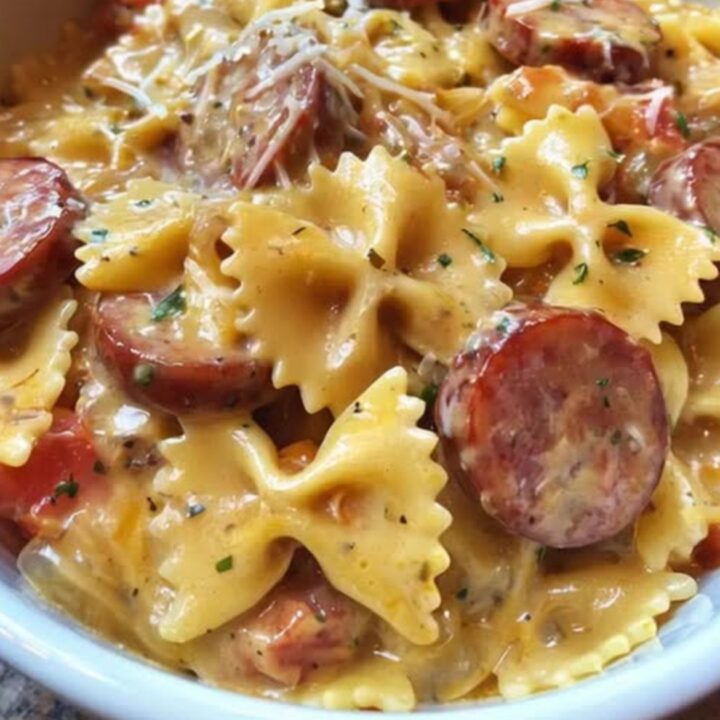 A white bowl filled with creamy farfalle pasta, seared smoked sausage coins, melted cheese, and fresh parsley.