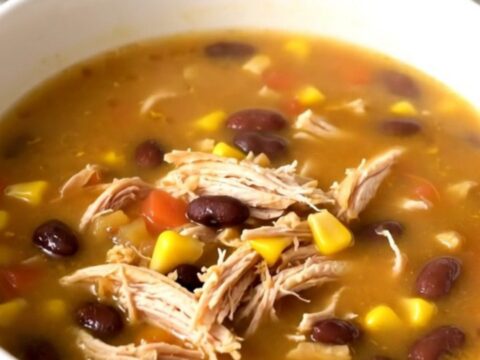A steaming bowl of Southwestern fiesta chicken soup with shredded chicken, black beans, and corn in a white bowl.