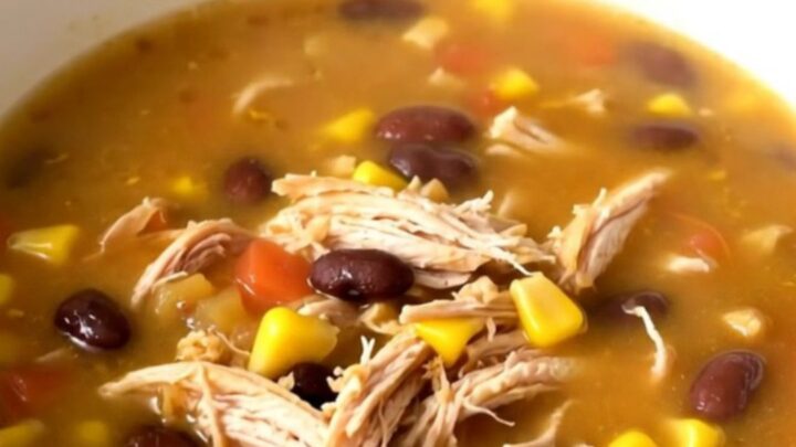 A steaming bowl of Southwestern fiesta chicken soup with shredded chicken, black beans, and corn in a white bowl.