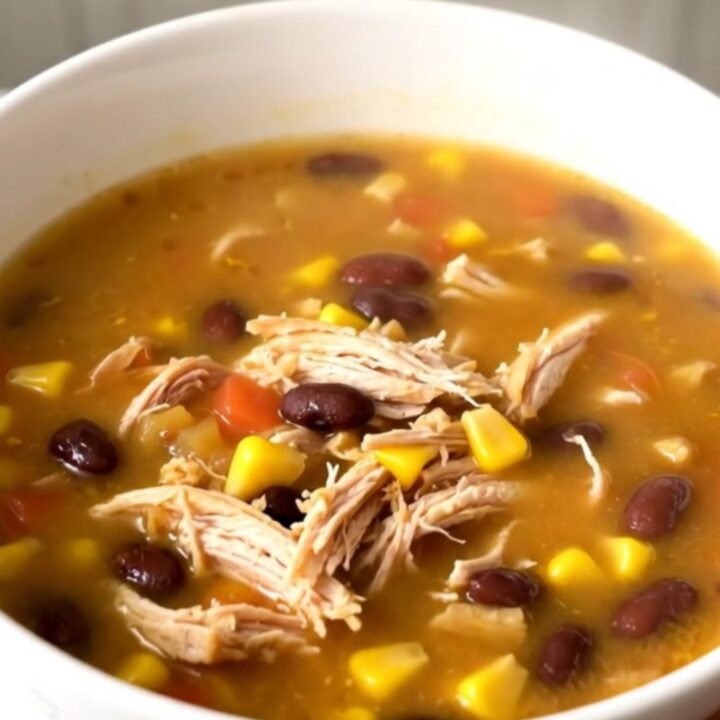 A steaming bowl of Southwestern fiesta chicken soup with shredded chicken, black beans, and corn in a white bowl.