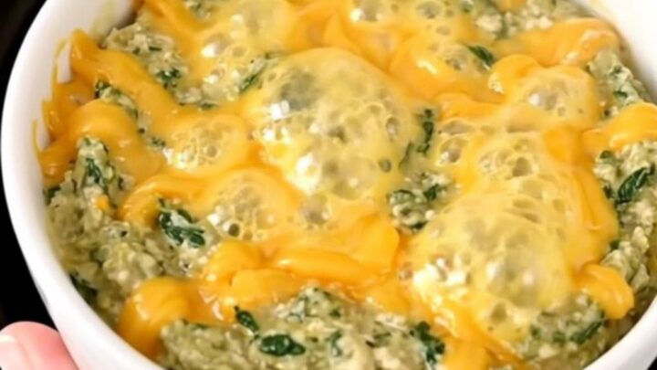 A top-down view of a black slow cooker filled with layers of spinach, bacon, and cream cheese ready to be cooked.