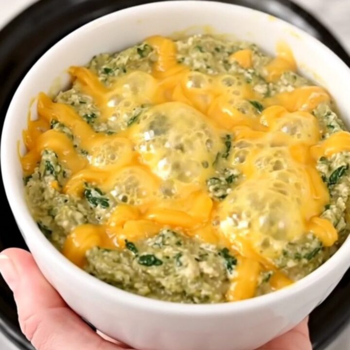 A top-down view of a black slow cooker filled with layers of spinach, bacon, and cream cheese ready to be cooked.