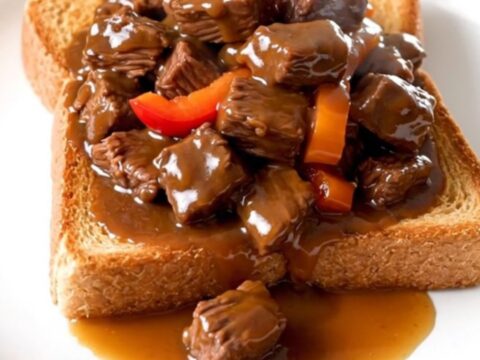 A plate of tender slow-cooked beef tips with peppers and onions over toasted Texas toast.