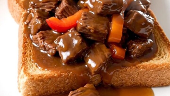 A plate of tender slow-cooked beef tips with peppers and onions over toasted Texas toast.