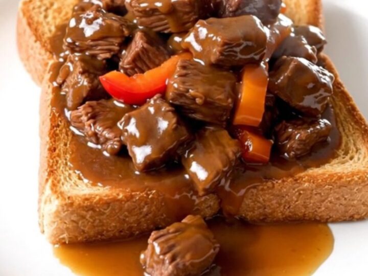 A plate of tender slow-cooked beef tips with peppers and onions over toasted Texas toast.
