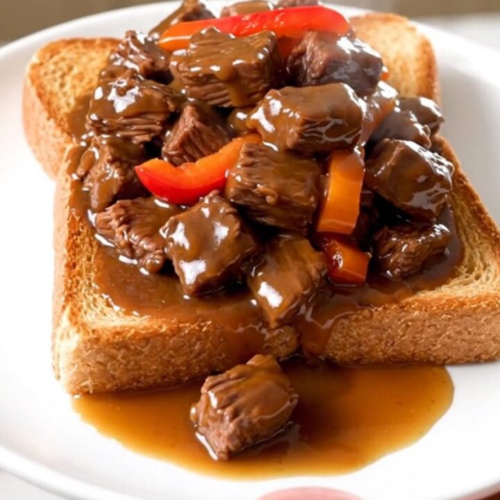 A plate of tender slow-cooked beef tips with peppers and onions over toasted Texas toast.
