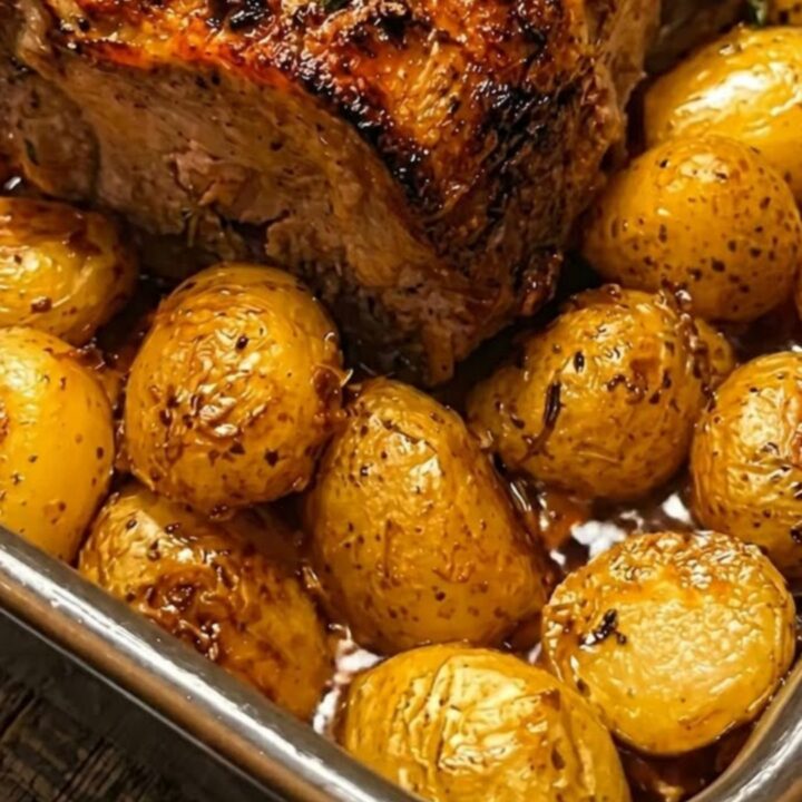 Perfectly roasted pork loin surrounded by glistening, blistered baby potatoes in a dark roasting pan