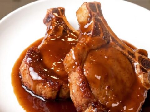 A plate of tender, glossy hoisin-glazed pork chops sitting on a white plate with a blurred kitchen background.