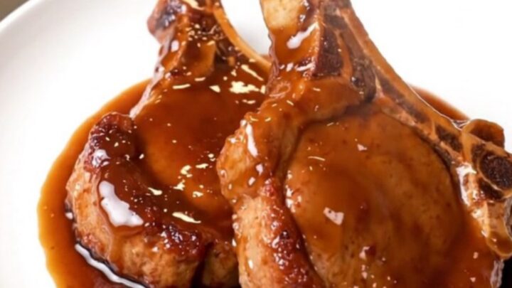 A plate of tender, glossy hoisin-glazed pork chops sitting on a white plate with a blurred kitchen background.