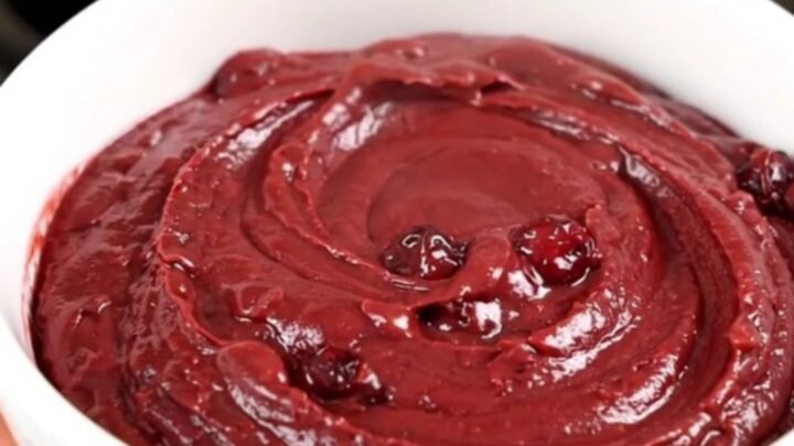 A top-down view of a crockpot filled with cubed brie, pecans, and cranberry sauce.