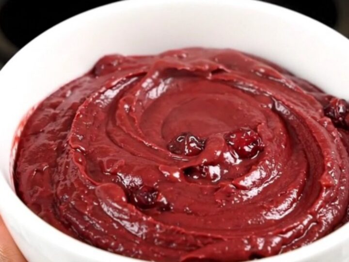 A top-down view of a crockpot filled with cubed brie, pecans, and cranberry sauce.