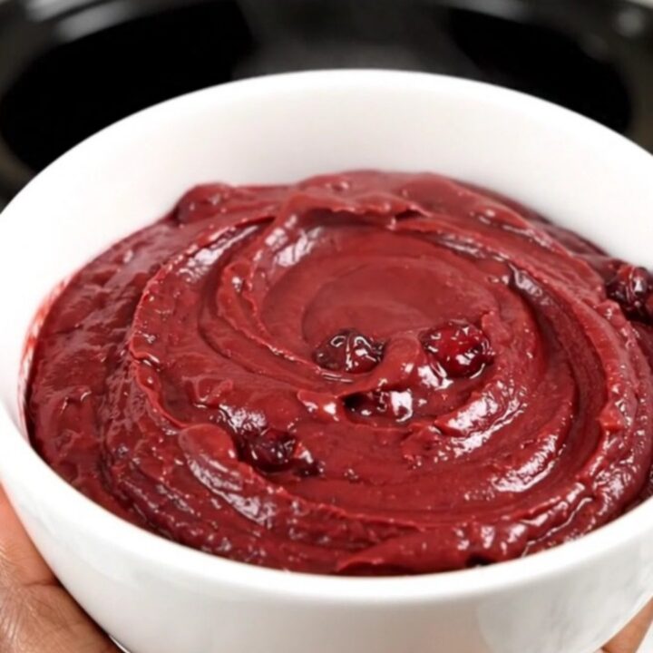 A top-down view of a crockpot filled with cubed brie, pecans, and cranberry sauce.
