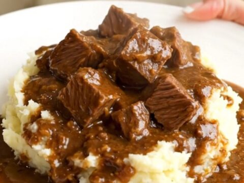 A close-up of a slow cooker filled with beef stew, showing tender chunks of beef and bright orange carrot slices in a rich