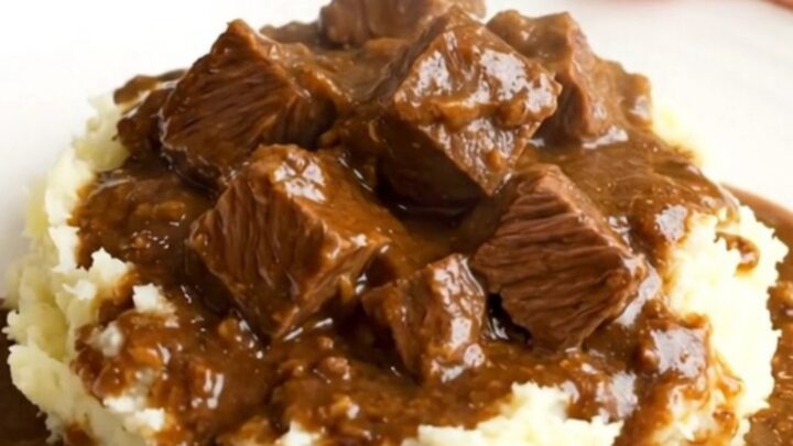 A close-up of a slow cooker filled with beef stew, showing tender chunks of beef and bright orange carrot slices in a rich