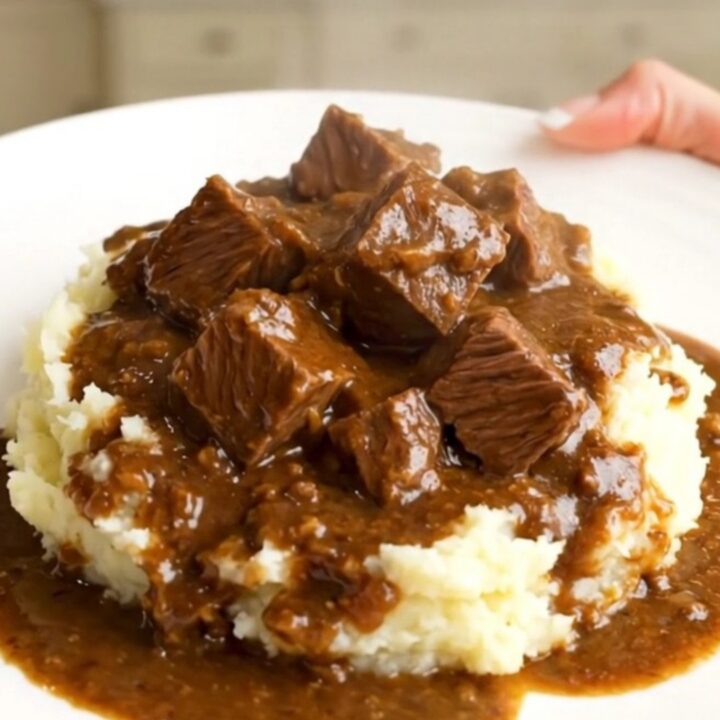 A close-up of a slow cooker filled with beef stew, showing tender chunks of beef and bright orange carrot slices in a rich