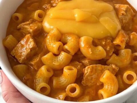 A steaming bowl of cheesy chili macaroni chicken with a rich, orange-hued sauce and tender chunks of chicken.