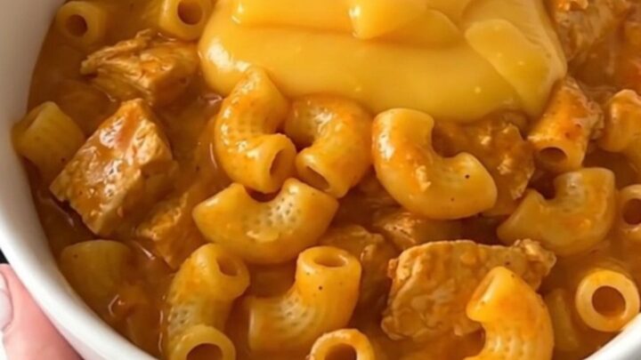 A steaming bowl of cheesy chili macaroni chicken with a rich, orange-hued sauce and tender chunks of chicken.