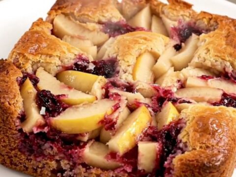 A golden, bubbling apple blackberry dump cake in a black oval slow cooker on a quartz countertop.