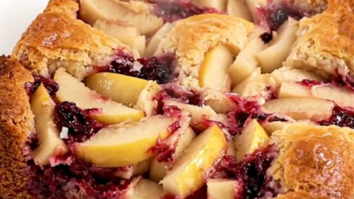 A golden, bubbling apple blackberry dump cake in a black oval slow cooker on a quartz countertop.
