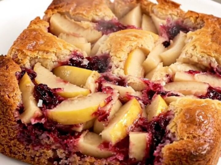 A golden, bubbling apple blackberry dump cake in a black oval slow cooker on a quartz countertop.