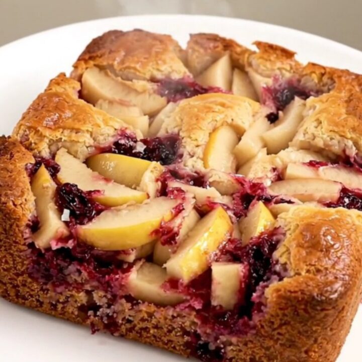 A golden, bubbling apple blackberry dump cake in a black oval slow cooker on a quartz countertop.