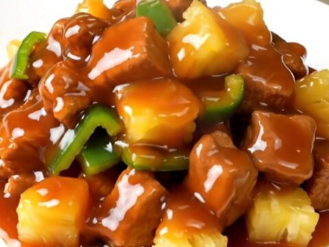 A plate of glossy, steaming sweet and sour pork loin with peppers and pineapple.
