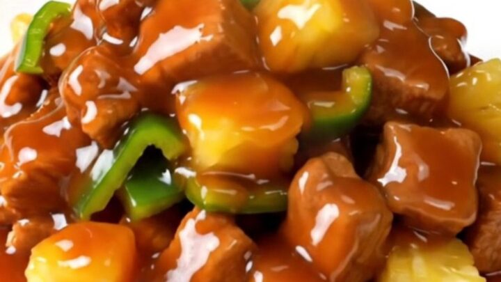 A plate of glossy, steaming sweet and sour pork loin with peppers and pineapple.