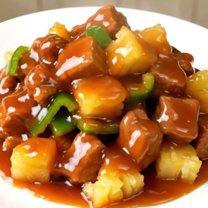 A plate of glossy, steaming sweet and sour pork loin with peppers and pineapple.