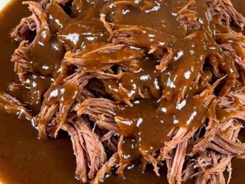 A close-up of a tender, shredded beef pot roast coated in a rich, creamy peppercorn gravy on a white plate.